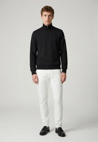 Black zip-up sweatshirt with a high collar and ribbed hem, paired with white fitted trousers and black loafers. Simple, clean design.