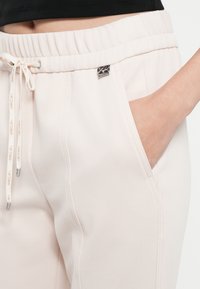 Hellrosa Jogginghosen mit strukturierter Oberfläche, elastischem Bund, verstellbarem Kordelzug und Seitentaschen. Kleines Markenetikett an der Tasche.