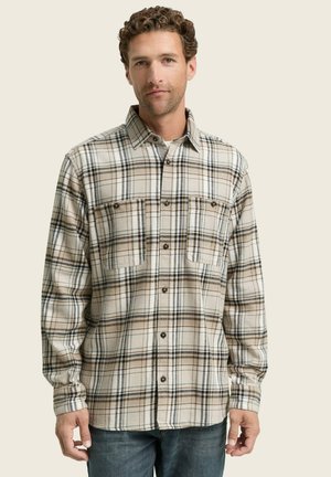 Chemise en flanelle à carreaux beige avec des lignes bleu foncé et marron, à boutons sur le devant, col pointu et deux poches sur la poitrine. Le tissu semble doux et texturé.