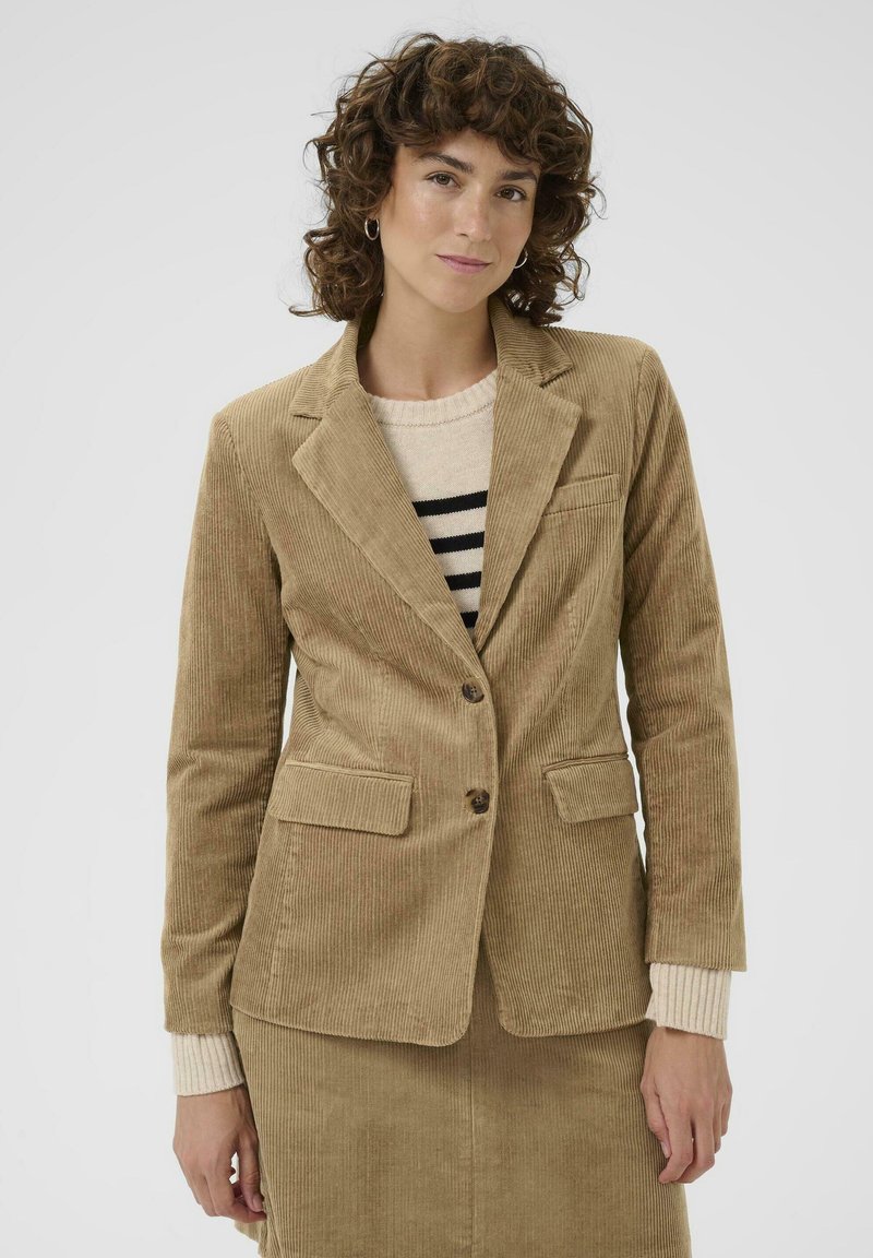 Blazer en velours côtelé beige avec une coupe ajustée, design à un seul bouton, revers crantés, deux poches avant et fermeture à bouton sur un fond neutre.