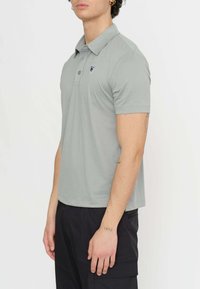 Polo shirt grigio a maniche corte con colletto classico, caratterizzato da un logo sul lato sinistro del petto e una texture di tessuto liscia e leggera.