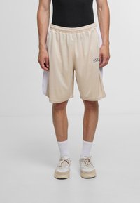 Beige Sportshorts mit weißen Seitenelementen, elastischem Bund und kleinem Logo auf der Vorderseite. Hergestellt aus leichtem, atmungsaktivem Material.