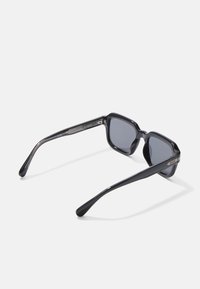 Juodi plastikiniai saulės akiniai su kvadratine apdaila ir pilkai tonuotais objektyvais. Su elegantiškomis, lenktomis rankenomis su metaliniais akcentais ir įspaustu prekių ženklu.