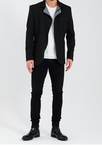 Czarna, dopasowana marynarka z szarym, wzorzystym wewnętrznym kołnierzem, pojedynczą kieszenią na piersi i dwoma kieszeniami z przodu, zestawiona z czarnymi, obcisłymi dżinsami oraz błyszczącymi butami.