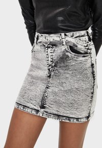 Mujer vestida con una blusa negra de manga larga de canalé metida dentro de una falda de mezclilla de tiro alto en un lavado ácido, con un cinturón de hebilla plateada.