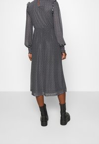 Czarna sukienka midi z długim rękawem w białe kropki. Posiada falbany na rękawach, elastyczny pas i dekolt w kształcie łezki. W zestawieniu z masywnymi czarnymi botkami.