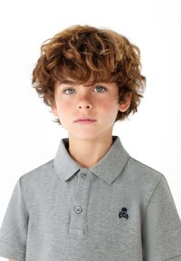 Polo gris avec col, comportant deux boutons et un logo de crâne bleu marine sur la poitrine gauche. Tissu doux et texturé, manches courtes.