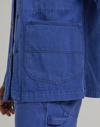 Blue striped jacket with a large back pocket. Made of sturdy fabric, featuring visible stitching and geometric patterns in the fabric texture.