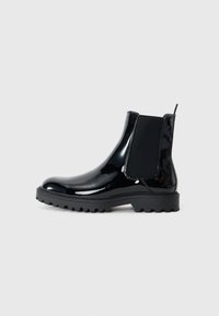 Botines de charol negro con paneles laterales elásticos, puntera redondeada, suela de goma texturizada y lengüeta en la parte trasera.
