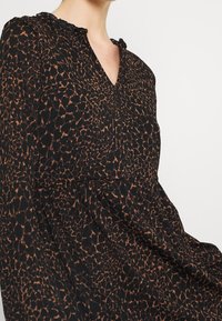 Svart klänning med ett leopardmönster i bruna toner. Har en V-ringning och volangkant vid kragen. Tillverkad i ett lättviktsmaterial.