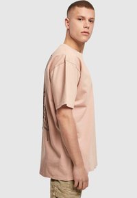 Light pink oversized T-shirt made of cotton. Features a graphic print on the back. Short sleeves and a relaxed fit. Plain front.