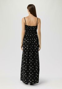 Zwarte maxi-jurk met witte abstracte patronen, voorzien van dunne bandjes en een gerimpeld lijfje. Vloeiende stof met een losse pasvorm.