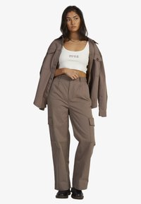 Brown cargo pants with pockets, paired with a white cropped top, and an oversized brown shirt jacket. Black footwear completes the look.