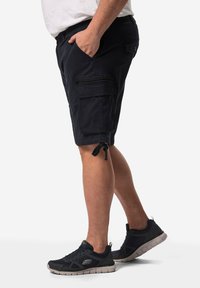 Námořnické cargo šortky se bočními kapsami, kapsou na zip, nastavitelným stahovacím lemem a lehkým materiálem, spárované s černými sportovními botami.