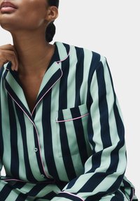 Set di pigiama a righe con ampie strisce verdi e navy e piping rosa. Include un davanti con bottoni e una tasca aperta sul petto per un tocco di stile.