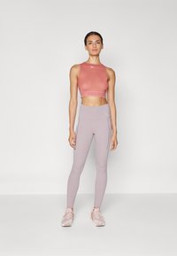 Ανοιχτό ροζ αθλητική μπλούζα cropped με λογότυπο στη ζώνη, συνδυασμένη με παστέλ μπορντώ κολάν ψηλόμεσα που διαθέτουν πλαϊνές τσέπες και λεία υφή.