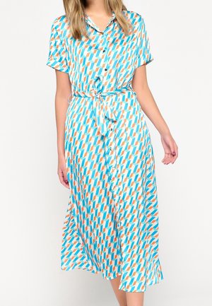 Femme portant une robe midi boutonnée avec manches courtes et motif géométrique bleu, orange et blanc, nouée à la taille.