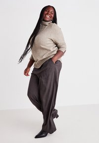Light gray sweater with a high neckline and three-quarter sleeves, paired with dark pinstriped wide-leg trousers and black heeled boots.