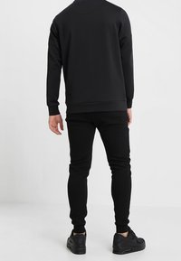 Black sweatshirt with a crew neckline and long sleeves, paired with matching black joggers and black sneakers. Fabric appears smooth.