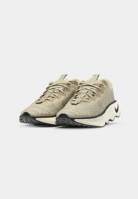 Beige løbesko med en tekstureret overdel og mønstret design. Har sort gummisål og signaturlogo på siden. Snørebåndslukning.