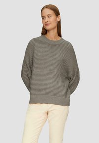 Grijze geribbelde trui met een ronde halslijn en verlaagde mouwen, met een brede zoom. Model draagt lichte broek.