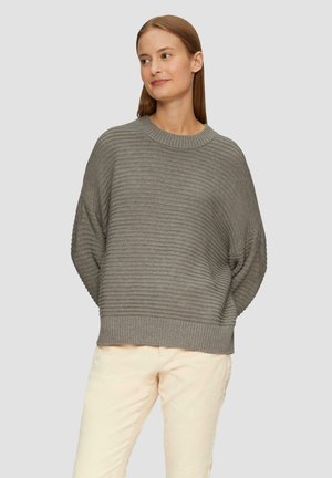 Grijze geribbelde trui met een ronde halslijn en verlaagde mouwen, met een brede zoom. Model draagt lichte broek.