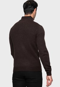 Maglione marrone a maglia con colletto alto, polsini a coste e orlo. Il tessuto testurizzato è spesso e aderente, ideale per essere indossato a strati.