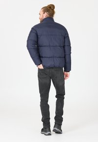 Doudoune marine avec un col montant, un design matelassé et des manches longues, assortie à un jean foncé et des baskets noires.
