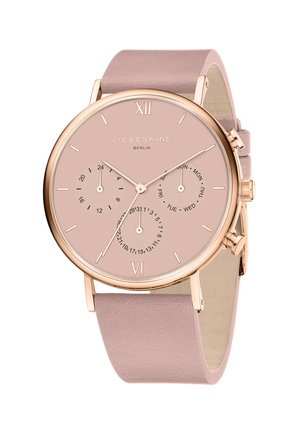 Rund pink ur med roseguld accenter, læderrem og tre understel for dato og dag. Har romerske talmarkeringer ved 12 og 6.