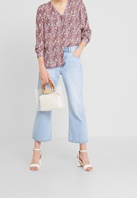 Blomstret bluse med lange ærmer i bordeaux, pink og creme; cropped lyse vaskejeans; gennemsigtig håndtaske med træhåndtag; hvide hæle.