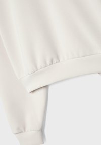 Hvid sweatshirtærme og kant med ribstrikkede manchetter på en ensfarvet lys baggrund.