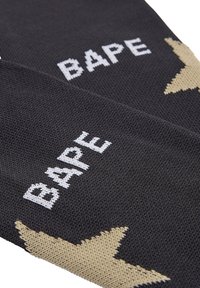 Schwarze gestrickte Socken mit weißem "BAPE"-Text und einem goldenen Sternmuster. Das Material ist strukturiert mit einer dichten Strickkonstruktion.