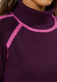 Strickpullover in dunklem Lila mit einem hohen Kragen. Mit markanten magentafarbenen geometrischen Akzenten an den Ärmeln und dem Halsausschnitt. Weicher Textur.