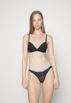 Reggiseno nero con bordi in pizzo e spalline sottili, abbinato a perizoma in pizzo nero con un elastico bianco di Calvin Klein.
