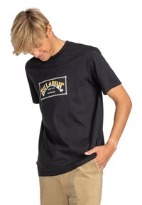 Black cotton t-shirt featuring a central graphic with the text "BILLABONG SINCE 1973 AUSTRALIA" in yellow and white, round neckline, short sleeves.