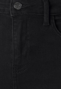 Jeans de mezclilla negra con cierre de botón metálico, dos bolsillos frontales y costuras en contraste. El material es suave y con un ligero estiramiento.