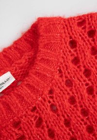 Czerwony sweter z dzianiny o teksturowanym, otwartym splocie. Posiada prążkowany okrągły dekolt oraz metkę na boku.