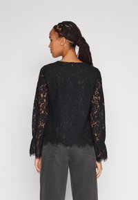 Black lace top with long flared sleeves, scalloped hemline, and back zipper closure, paired with dark gray wide-leg pants.