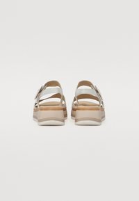 White platform sandals with a thick beige sole, featuring two adjustable straps and a rounded back for support. Smooth leather texture.