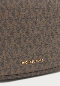 Brązowa tkanina o teksturowanej powierzchni, z powtarzającym się wzorem, z złotą metką "MICHAEL KORS" na dole.