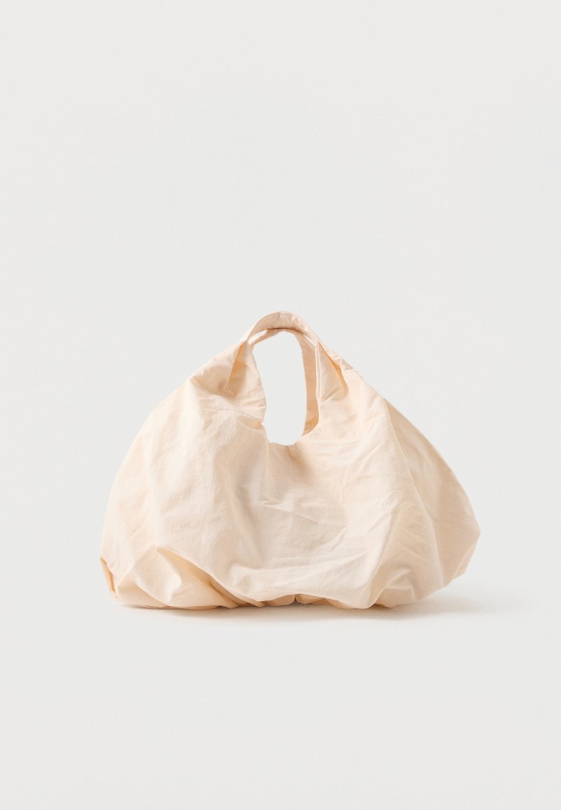 Béžová opakovane použiteľná taška z textilu s zaobleným tvarom a integrovanými krátkymi rúčkami, zobrazená na jednoduchom bielom pozadí.