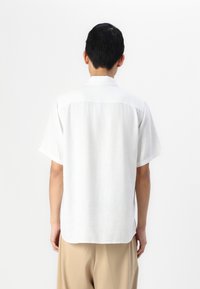 Witte shirt met korte mouwen, lichtgewicht linnen stof, iets relaxed fit, subtiele textuur, afgeronde zoom, standaard kraag, details aan de achterkant.