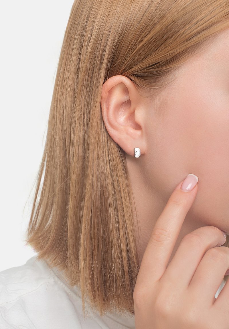 Silverfärgade studörhängen med rektangulär form, med texturerad detaljering och en polerad yta, som bärs på en models öra.