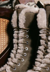 Zielone buty z futerkiem syntetycznym i sznurowanym designem. Widoczne srebrne oczka i teksturalne detale materiału, które podkreślają dopasowanie.