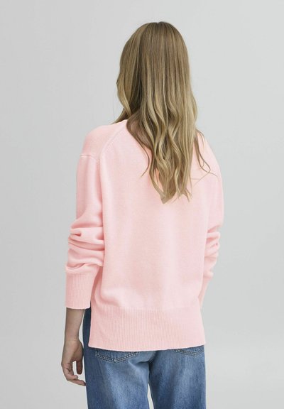 Heled roosa kootud särk, millel on soonikuga varrukad ja hem, lõdva lõike ja langenud õlgadega. Kandmine siniste teksade peal. Tagumine vaade.