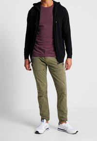 Black zip-up hoodie, maroon t-shirt, olive green cargo pants with pockets, and white sneakers with navy accents. Casual outfit displayed.