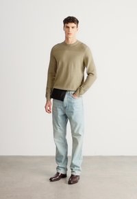 Długa koszula z dzianiny w kolorze oliwkowej zieleni, jasnoniebieskie dżinsy i ciemnobrązowe skórzane buty. Prosty, luźny krój z minimalnymi zdobieniami.