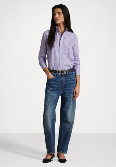 Helles lila Hemd mit Knopfleiste, hoch taillierte blaue Jeans, schwarzer Gürtel mit silberner Schnalle und schwarze Absatzschuhe. Glattes Material und lockere Passform.