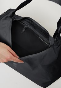 Borsa tote nera realizzata in materiali riciclati, con chiusura superiore con zip, texture liscia e dettaglio del logo di lato.