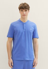 Modrá polokošile s krátkým rukávem a zapínacím límcem, vyrobená z měkké bavlny. Na levé straně se nachází malé logo.